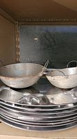 Eight metal charger plates with beach-themed raised design and two metal bowls with wire handles placed on a shelf.