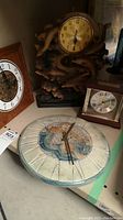 Photo showing all three clocks together: the round ceramic wall clock with artistic design in foreground, large resin dolphin wall clock in back, and small Bulova desktop clock beside it.