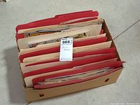 View of the cardboard box filled with red and beige folders containing comic books shown from a front angle.