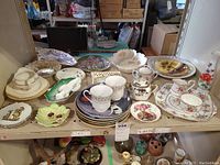 Overview of assorted dishware including plates, trays, cups, creamers, sugar bowls, and vase arranged on a table, showing variety of patterns and some visible wear.