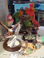 Front view of all six animal figurines including American eagle, colorful parrots on branches, owl, and lion on textured bases.