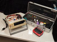 Overall lot: multimeter on stand, aluminum case with charger, batteries, spray bottles and spool of wire