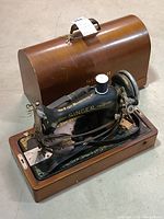 Singer sewing machine in wooden base with dust cover sitting behind it on floor.