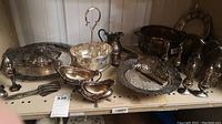 Shelf display showing various silverplate serving items including salt and pepper shakers, trays, tongs, and pitcher.