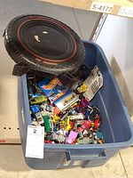 Blue bin filled with various toy cars and Hot Wheels carrying case lid shaped like a tire.
