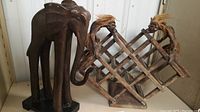 Side view of the wood wine rack with two carved tribal figures and a carved elephant figure on a black base.
