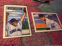 Photo showing two vintage baseball cards: Alfonso Carrasquel #60 and Alex Kellner #57 on a textured surface.