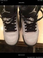 Top-down view of Air Jordan Retro 5 sneakers showing white leather upper, black tongue with Jumpman logo, and black laces with translucent lace locks.