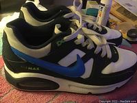 Side view of the left sneaker showing black upper with white mesh and blue Nike Swoosh, Air Max branding visible on sole.