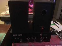 Photo of the black Bluetooth audio tuner and amplifier with two black speakers on top, showing the front control panel and top surfaces.