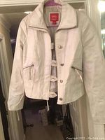 Front view of white leather jacket on hanger showing zipper and buttons.
