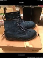 Side view of blue suede Dr Martens boots showing profile, laces, sole and brand details on box.