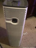 Front view of the white Holmes tower air purifier with honeycomb-style grille and control panel display, placed on carpeted floor.