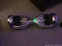 Silver hoverboard with black footpads and green central light on carpet background