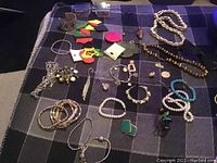 Photo of assorted costume jewelry items including bracelets, earrings, necklaces, and rings spread out on a fabric surface.