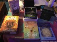 Overview photo showing all card decks in their boxes and some cards spread out, including Casanova Tarot, Barbieri Zodiac Oracle, Spirit Animal Oracle, Practical Witch Tarot, and a pack of tarot cards with a Five of Chalices card on top.