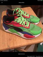 Pair of men's Puma sneakers with green, red, blue, white colors and neon green laces shown at side angle on wooden surface