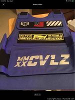 Front view of blue motorcycle vest with multiple patches and white MMXXCVLZ text