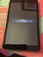 Front view of black Nextbook tablet turned on showing logo on startup screen with visible cracks.