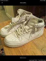 Side view of both white Nike Air Force 1 Mid sneakers showing perforated toe box, ankle strap, and leather upper.