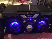 Front view of Sylvania Bluetooth speaker with glowing blue LED lights and connected USB cable.