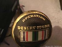 Close-up of walking cane handle with Operation Desert Storm emblem and ribbon bar detail