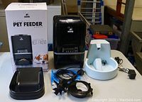 Automatic pet feeder with control panel, accessories, packaging, and water fountain placed on a table