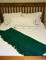 Bed dressed with cream damask coverlet and matching pillow shams, heavy dark green throw folded on bed