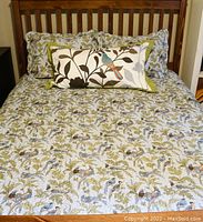 Queen bed made with lightweight coverlet and two matching queen shams featuring bird and branch print on muted color background.