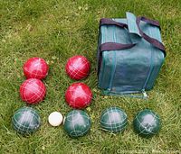 Eight bocce balls (four red, four green) arranged on grass next to a green fabric carry case with zipper and handles.