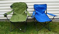 Front view of two camp chairs, one green and one blue, showing fabric seats with armrests and built-in cup holders.