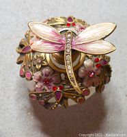 Top view of perfume bottle showing dragonfly design in pink enamel and clear gems with floral accents in red and purple enamel and gems.