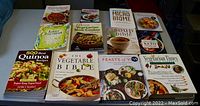 Full view of ten cookbooks by various authors on vegetarian and healthy cooking, laid flat on a gray surface.