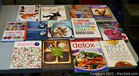 Photo showing 15 cooking and health books arranged on a table featuring titles on cooking, detox, Superfood smoothies, quinoa, oats, wheat belly, spa recipes and energy bites.