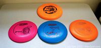 Top view of four discs laid out: pink, blue, orange disc golf discs, and one orange frisbee showing logos and designs