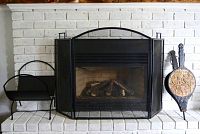 Fireplace showing the three-panel mesh fireplace screen in front of the gas fireplace, with a semi-circular log rack to the left and decorative bellows to the right.