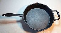 Full view of the black cast-iron frying pan showing the long handle and helper handle, with no visible damage.
