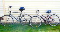 Both man's and woman's bicycles side by side outdoors against house siding with helmets placed on seats.