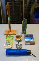 Photo showing all items arranged on table including the wooden jewelry stand, compass, pottery dish, umbrella, bird-shaped candle, Christmas ornament, and box of playing cards.