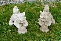 Pair of cast-concrete temple (foo) dogs placed on grass showing overall size and posture.