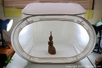 Oval collapsible light box with white translucent fabric for diffused lighting, setup indoors with a small wooden statue inside to demonstrate use.
