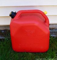 Red plastic gas can outdoors, front side showing capacity markings and handle.