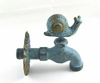 Side view of outdoor faucet showing snail handle and chrysanthemum wall flange with verdigris finish.