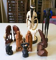Full group shot of nine wooden carvings and alabastrite statue including the flapper with wolfhound and various animal and human figures.