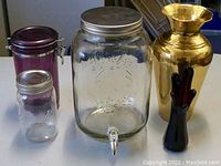 Four items: two glass storage jars, one brass vase, one hand-shaped decorative glass vase