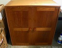 Front view of teak veneer cabinet showing two closed doors with wooden knobs and a uniform wood finish.