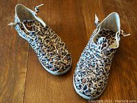 Top-down view of the pair of women's leopard-print woven leather Huarache boots on wooden floor showing intricate weaving and overall condition.