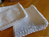 Close-up photo of two white napkins showing detailed floral embroidery and lace scalloped edges.