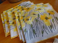 Eight folded napkins showing the yellow floral design stacked neatly on a wooden surface.