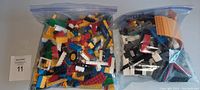 Two bags of assorted LEGO pieces with many colors and shapes including wheels and structural bricks